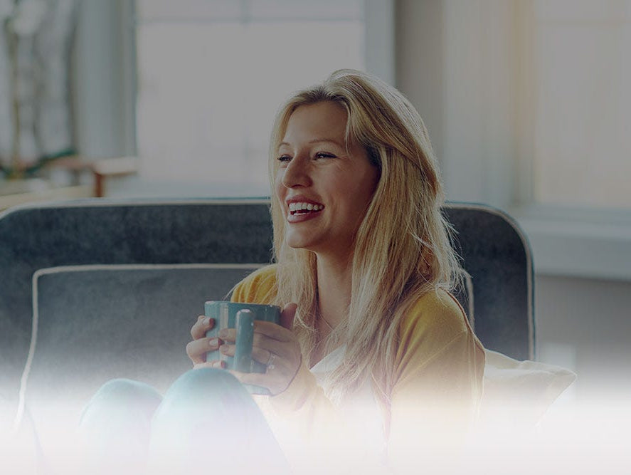 Smiling women, sitting in an oversized chair, holding a coffee cup.