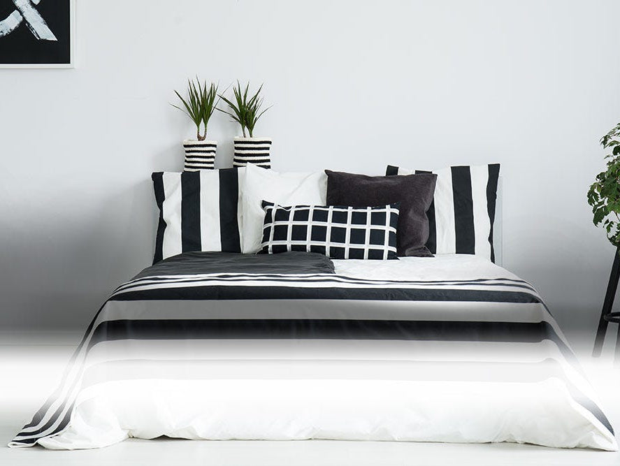 Bedroom set consisting of bed with monochrome bedspread and pillows and plants in black and white planters.