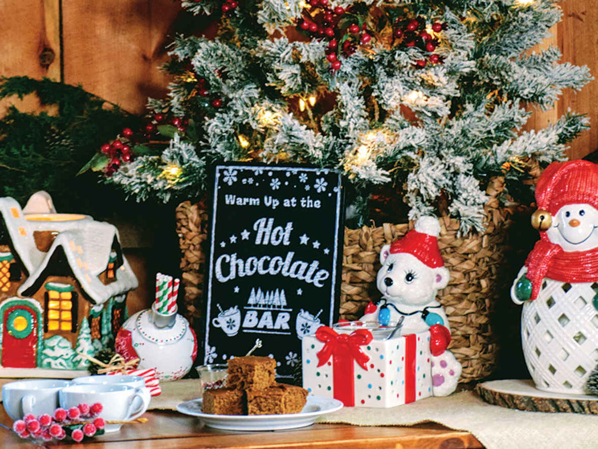 A variety of Christmas themed candle holders in front of a frosted Christmas bush.