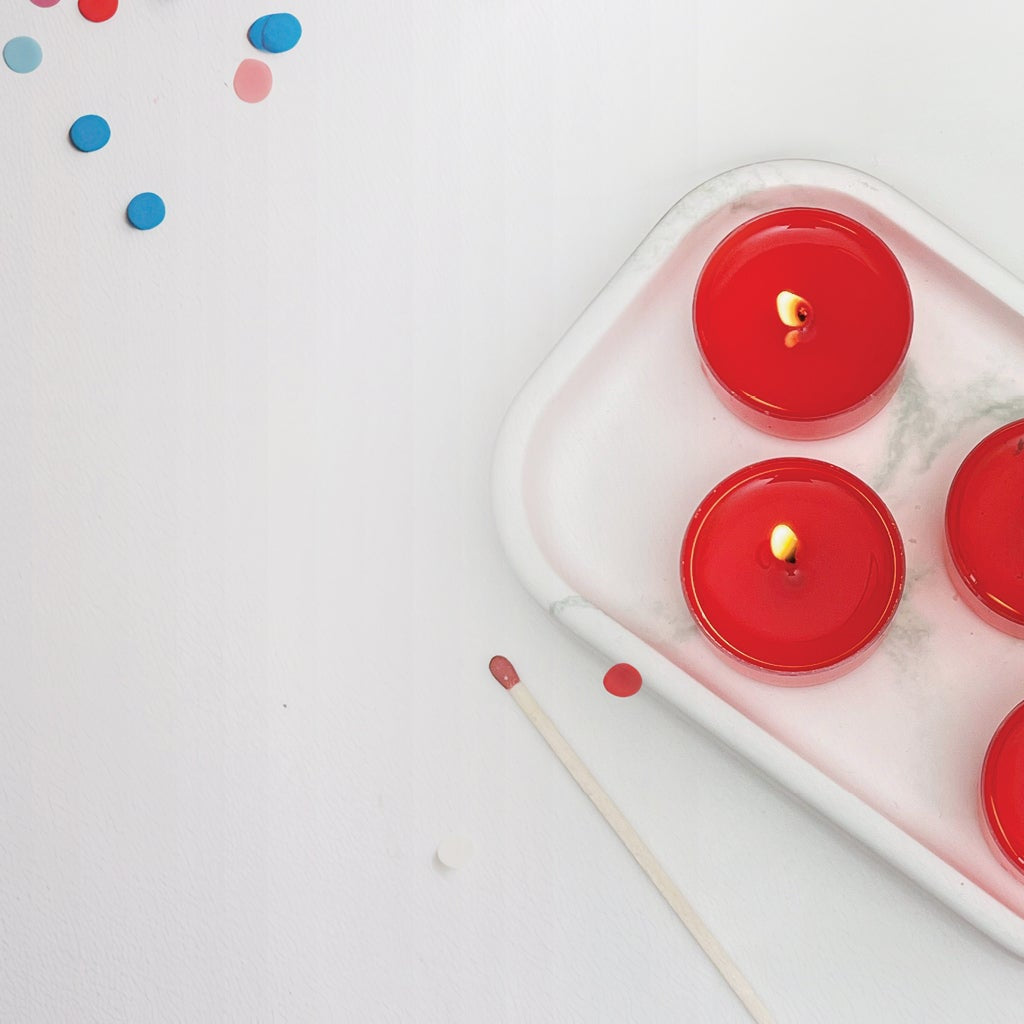 4 red tealight candles on a dish, confetti scattered on table.