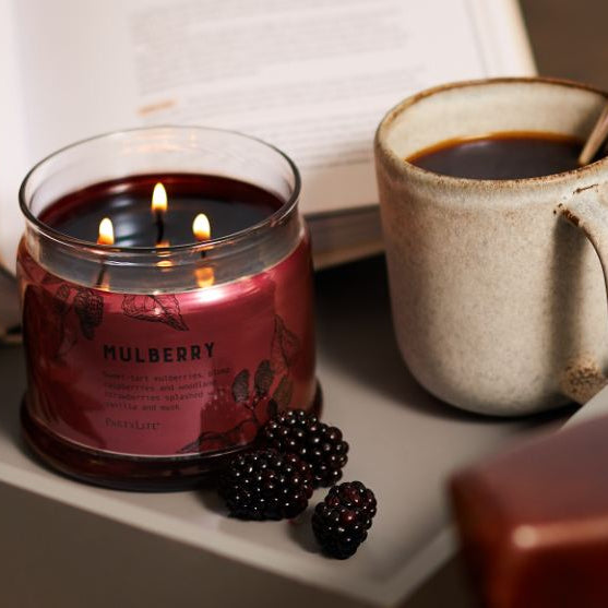Dark brown 3-wick cancel on tray with book and beverage.