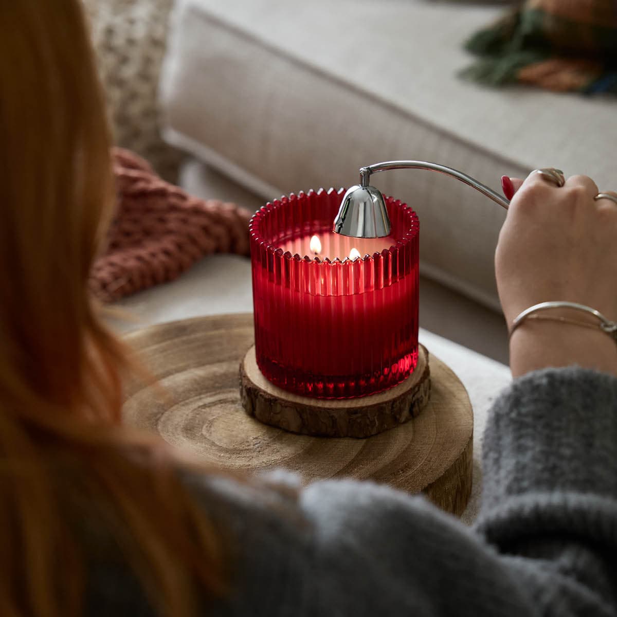 Mulberry Specialty Jar Candle red jar with 2 wicks shown lit with a lady holding the chrome snuffer just above it.