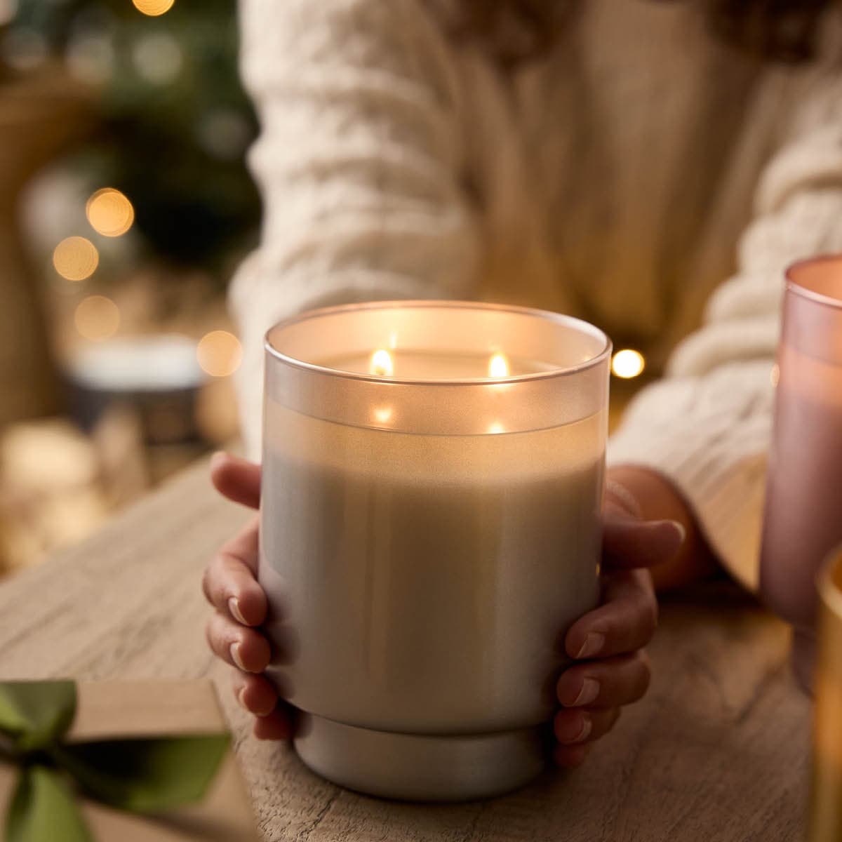 Cinnamon & Bayberry 2-Wick Specialty Jar Candle shown with a person's hands other side of the jar on a wooden surface.