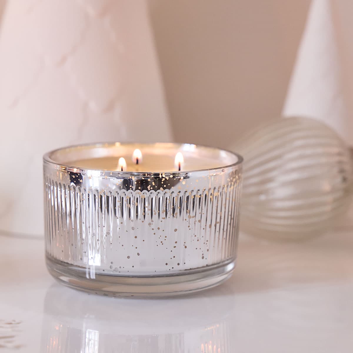 Winter Morning 3-Wick Ripple Jar Candle lit next to a Christmas Bauble the Jar is silver color and the wax is white.