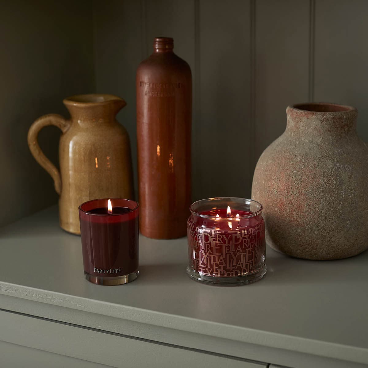 Tamboti Woods Escential Jar candle lit shown next to 3-wick jar candle also lit with a decorative bottle and vases.