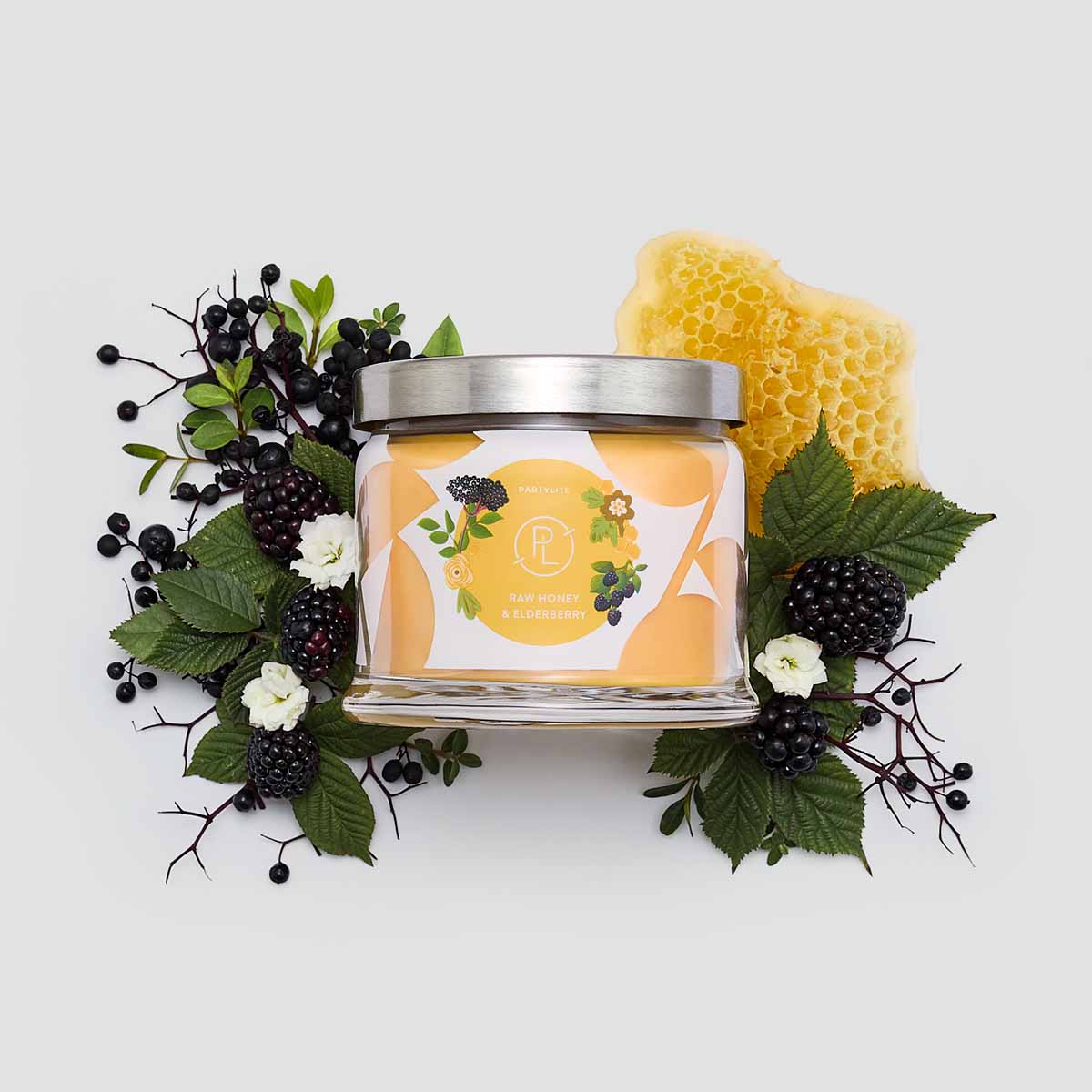 Raw Honey & Elderberry 3-wick Jar Candle with berries, honeycomb and leaves surrounding it against a white background.