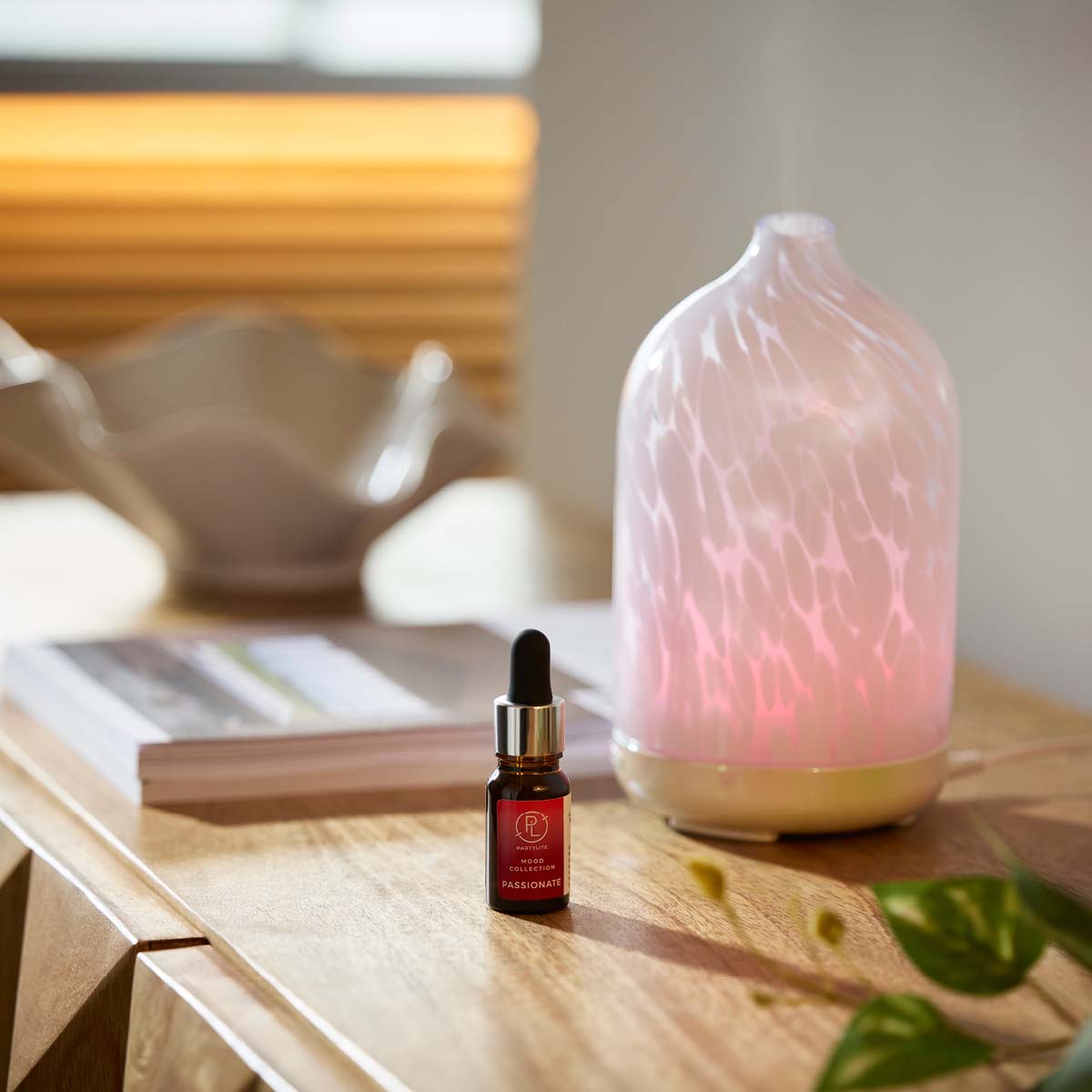 Passionate Fragrance Oil from the Mood Collection next to a fragrance diffuser on a wooden surface with a blurred book in the background.