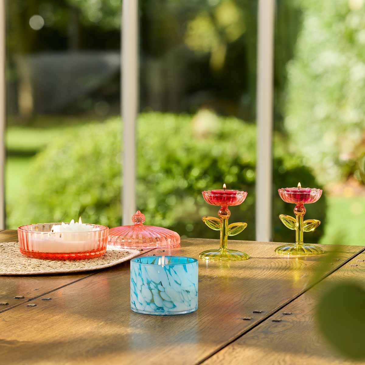 Sea and Sky Large Tealight Holder with a Garden Party Jar candle lit in the background on a wooden surface.
