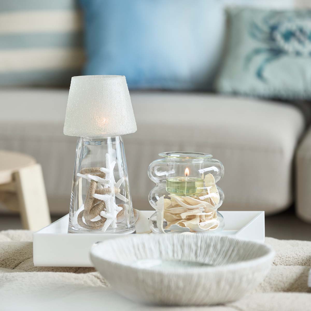 Clearly Creative Tealight Lamp shown with a tealight holder with a lit tealight on a white tray with a blurred sofa in the background.