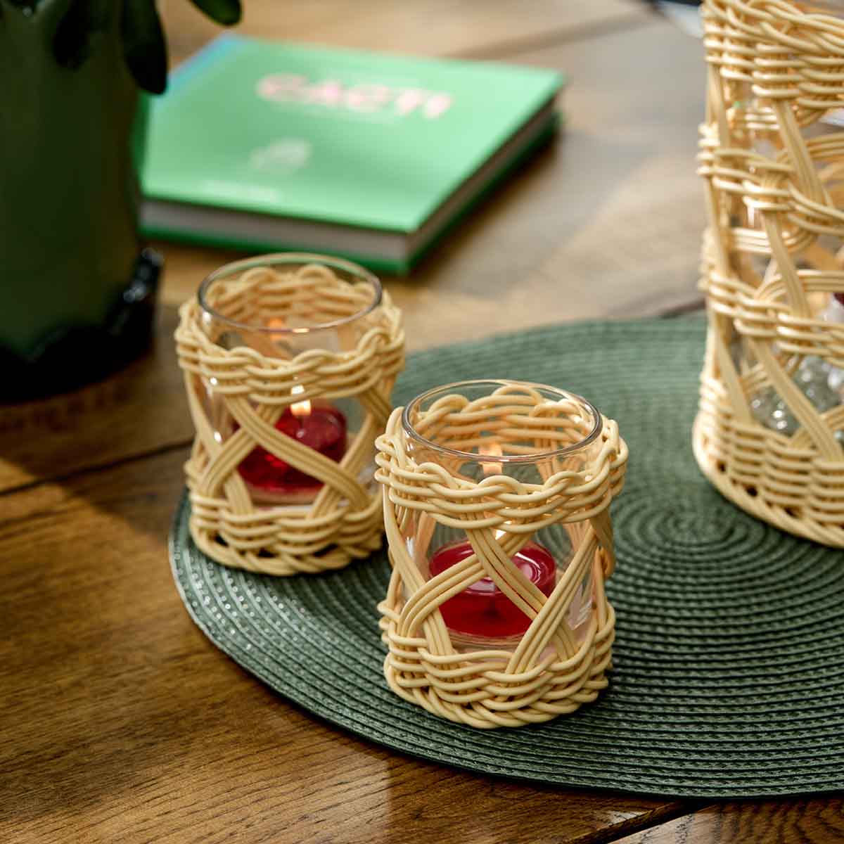 Woven Tealight/Votive Holder shown on a green woven table mat on a wooden table with a book in the background.