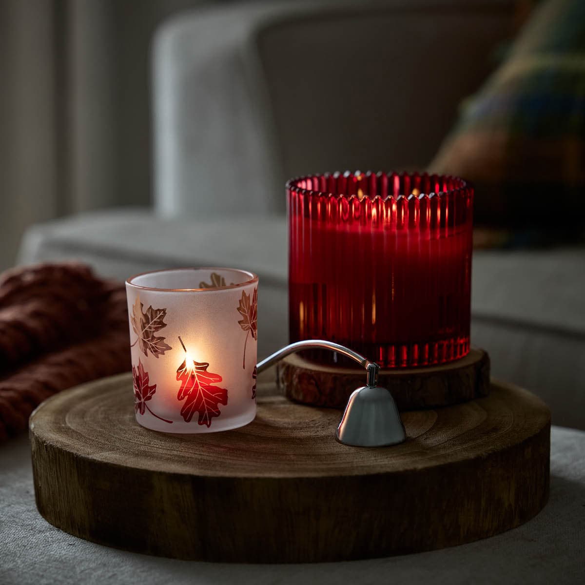 Mulberry Specialty Jar Candle lit shown with an Autumn Leaves Tealight holder with a chrome snuffer in between them on a wooden round surface.