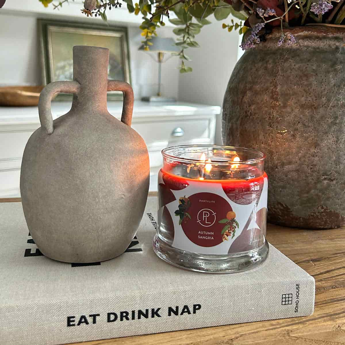 Autumn Sangria 3-wick Jar candle lit sitting on a book next to a vase.