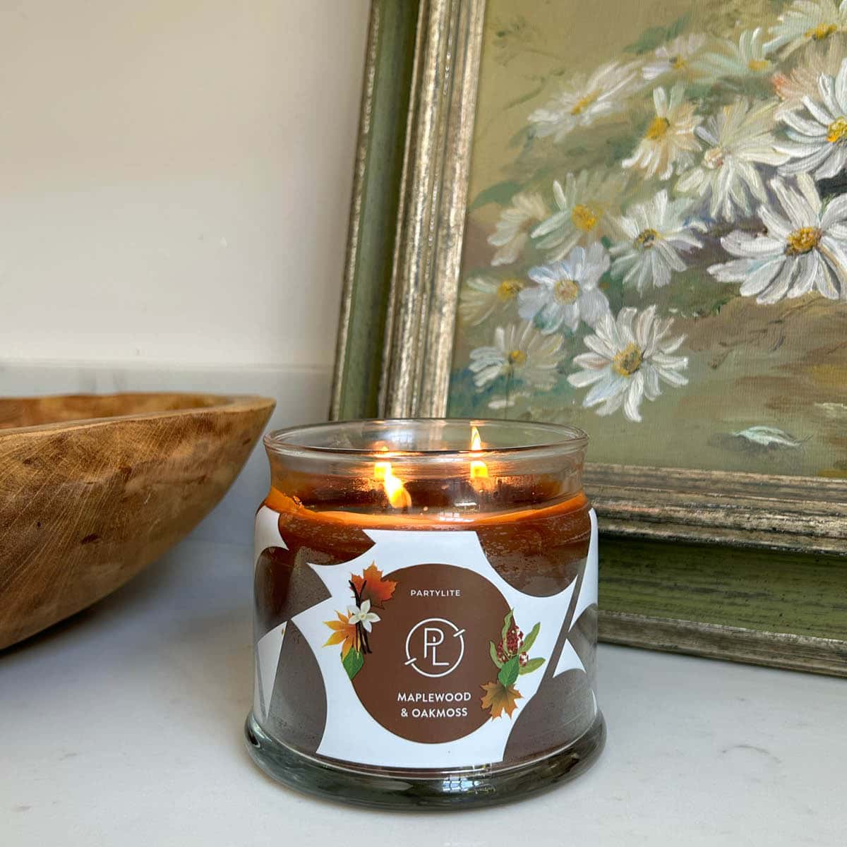 Maplewood & Oakmoss 3-wick Jar Candle lit with a picture of flowers in the background.