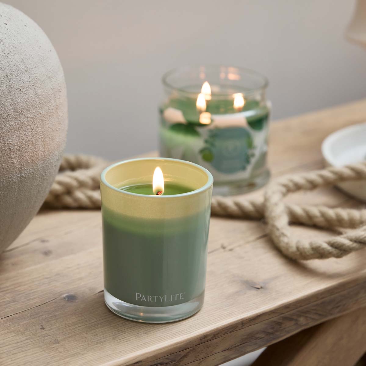 Seagrass Eucalyptus Escential Jar™ Candle on a wooden surface with rope behind it and the a 3-wick jar candle blurred in the background.