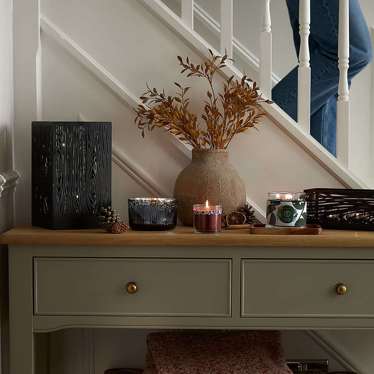 Wood Grain Hurricane shown with a Ripple Jar Candle, Mini Jar Candle and 3-wick Jar candle all lit on a hallway cabinet with stairs in the background.