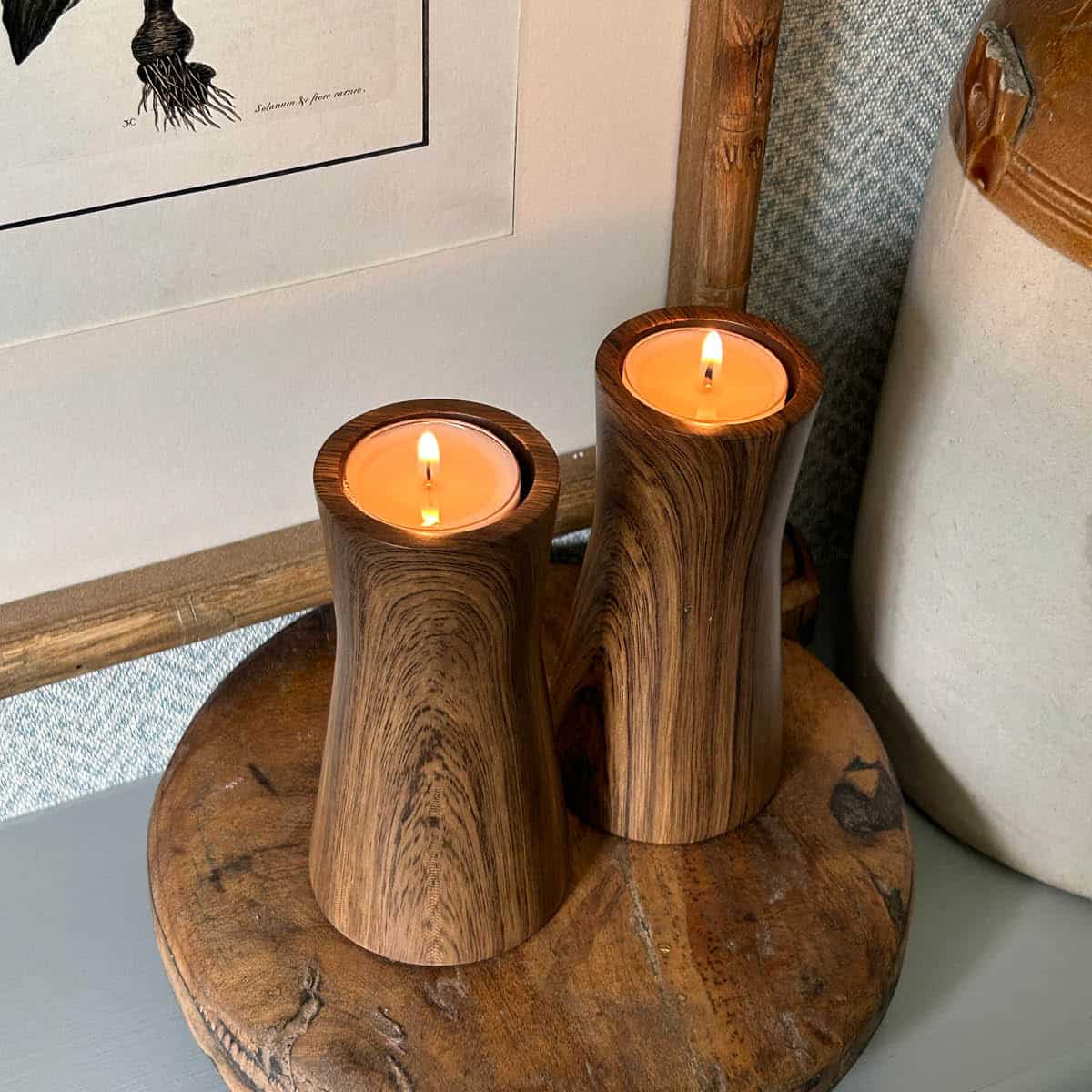 Faux Bois Tealight Holder Pair with lit tealight candles on a wooden coaster.