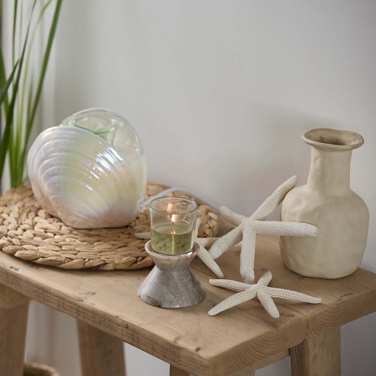 Unity Stone Candle Holder on a wooden table with a Shell Scent Warmer with star shaped decorative items and porcelain vase against a light background
