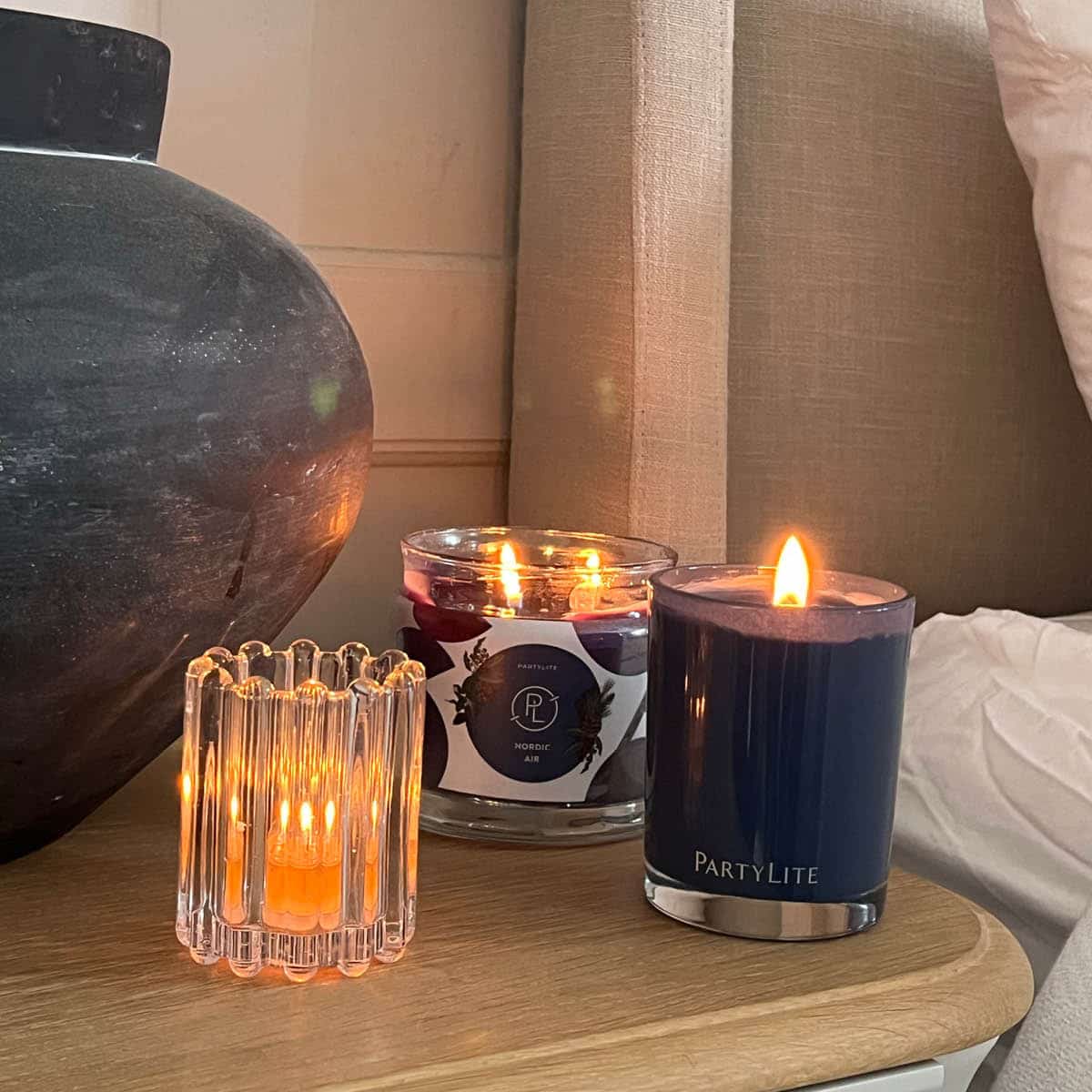 Ripple Glass Tealight/Votive Holder Pair clear glass with a lit candle shown with a lit Escential jar, 3-wick Jar candle on a wooden surface