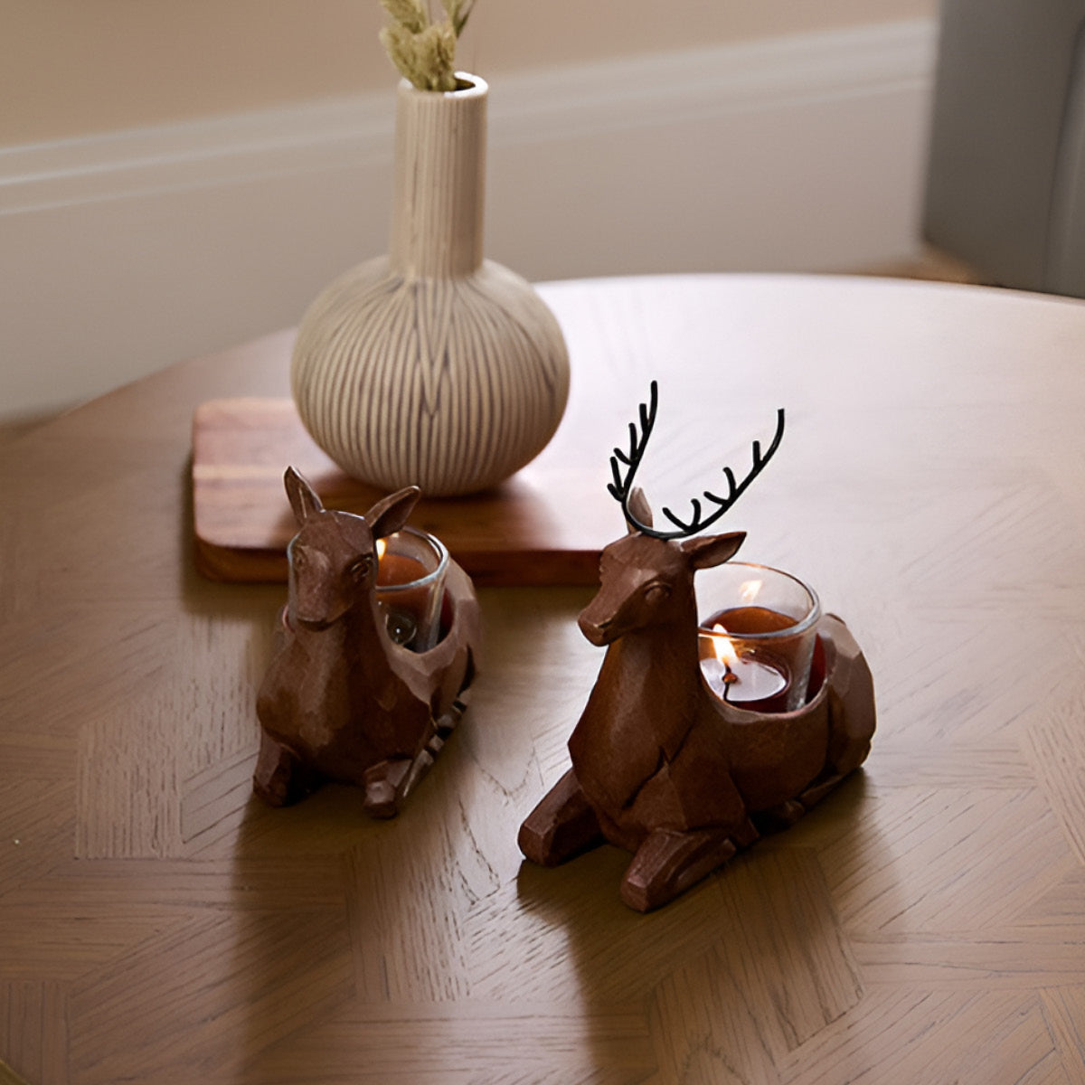 Carved Deer Tealight holder pair shown on a wooden table top with a vase in the background