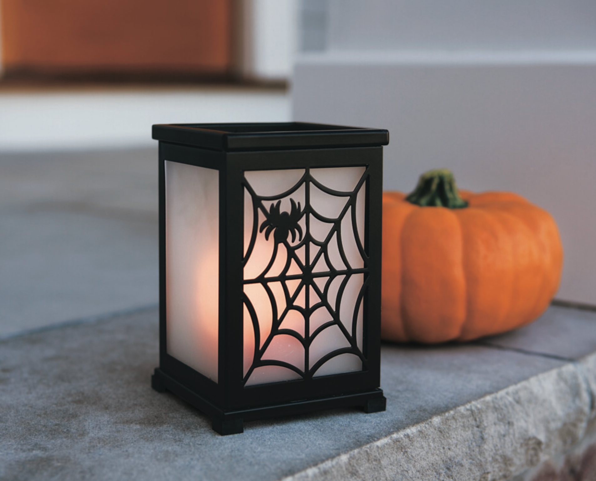 Change-O-Luminary Candle Holder shown with a spider web and spider on one side of the hurricane with a Pumpkin next to it.