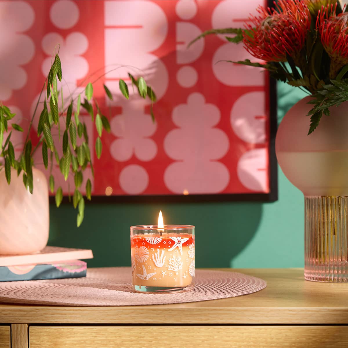Grapefruit Peach Paloma Mini Jar Candle on a pale pink woven table mat on a wooden surface with a orange/pink wall art against a green wall with vases of flowers next to the Mini Jar