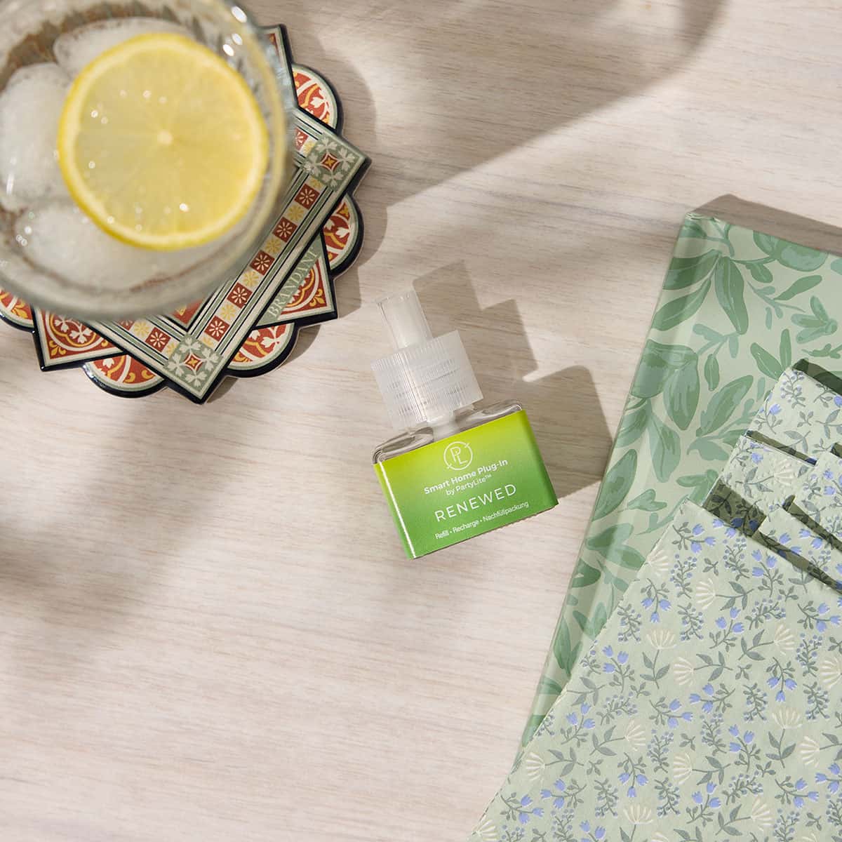 Renewed Smart Home Plug In Refill against a light grained wooden surface with colorful coasters with a glass of ice and Lemon and other decorative coasters