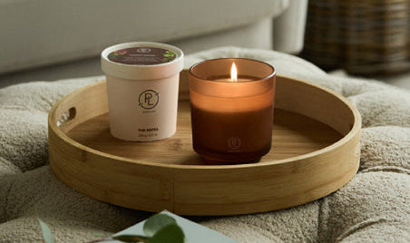 Refillable candle jar and refill candle on a wooden tray with a blurred background of a living room
