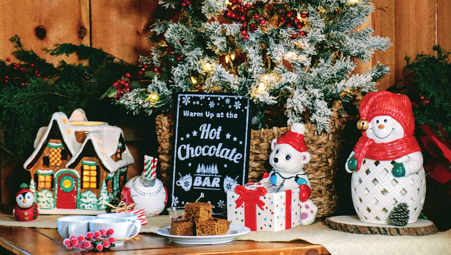 A variety of Christmas themed candle holders in front of a frosted Christmas bush.