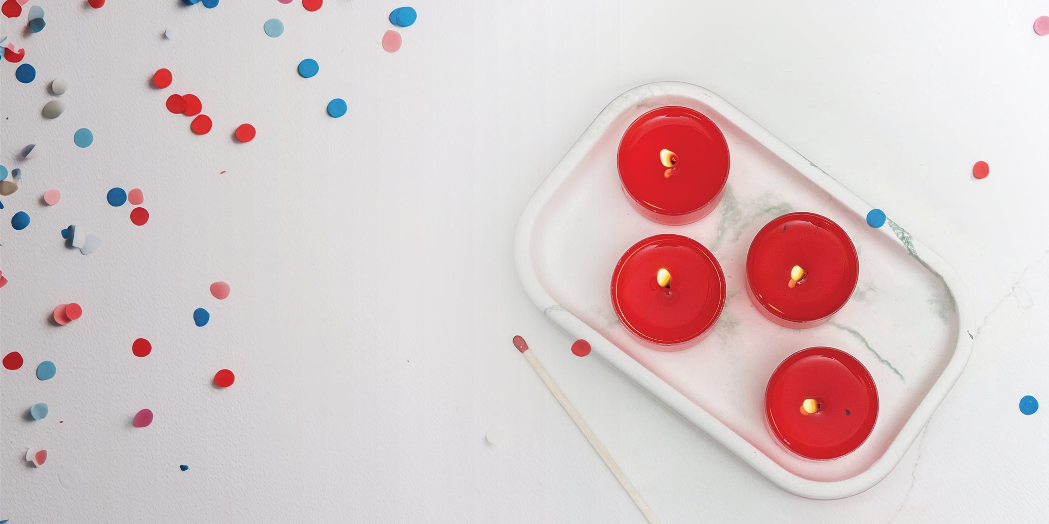 4 red tealight candles on a dish, confetti scattered on table. 
