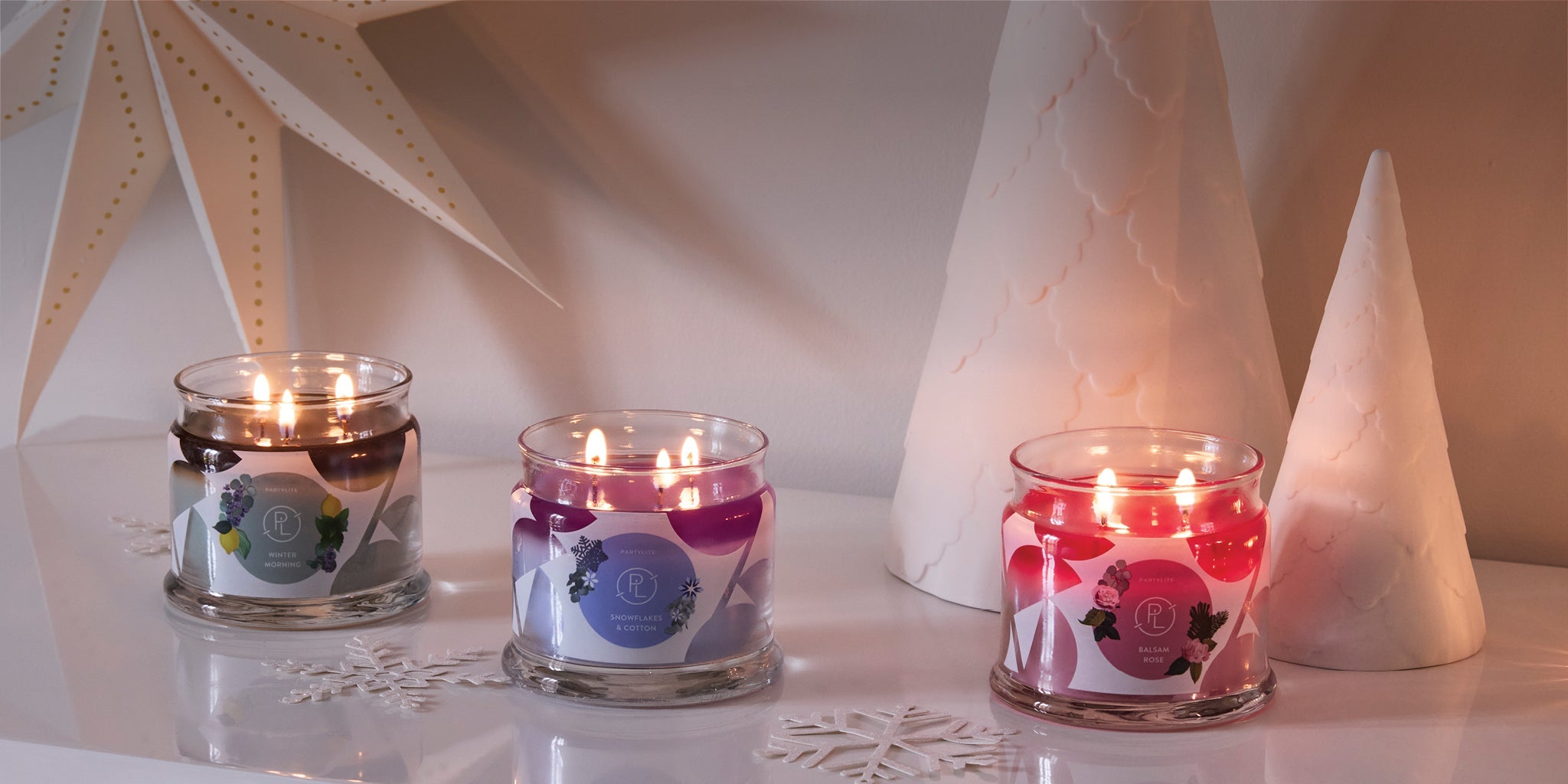 Three 3-Wick Jar candles with decorative white trees on a table. 