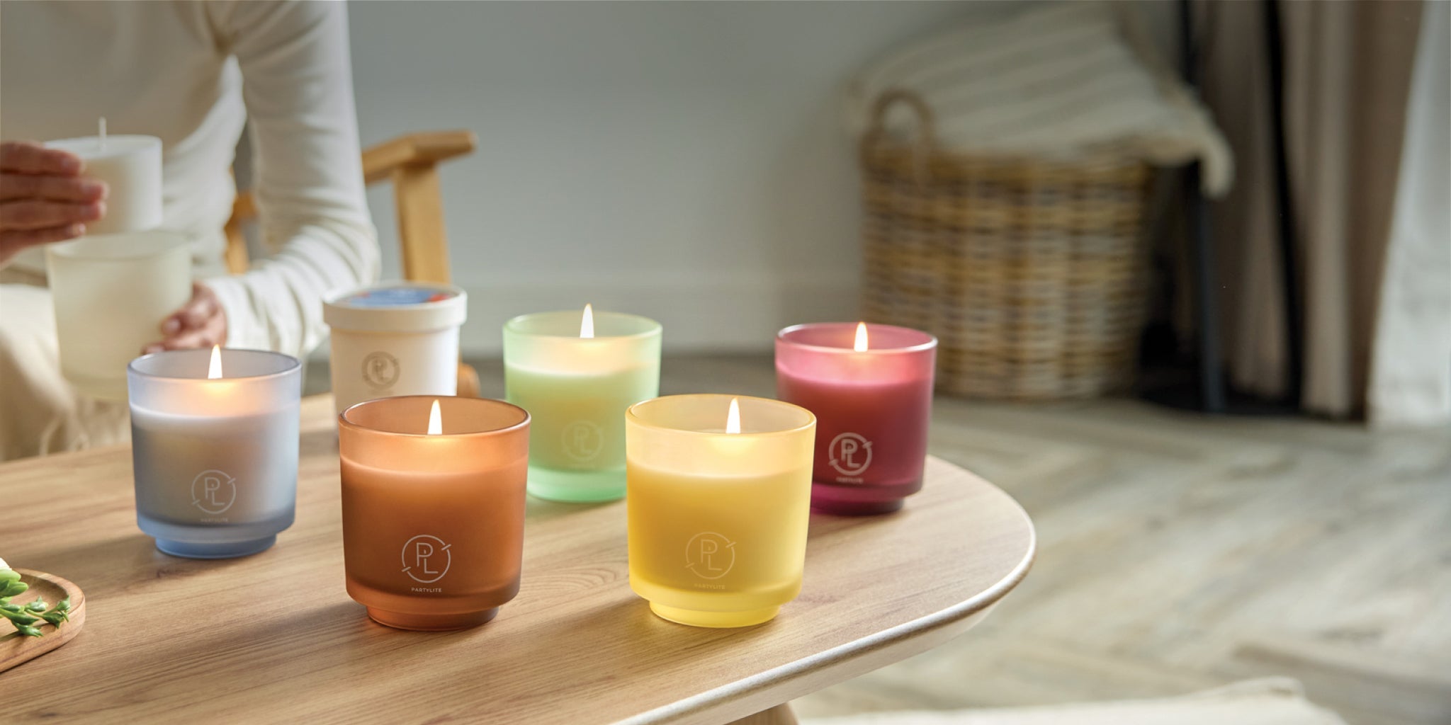 Coffee table with 5 Refillable Jar Candles and one Refill. Person in background is refilling a candle. 