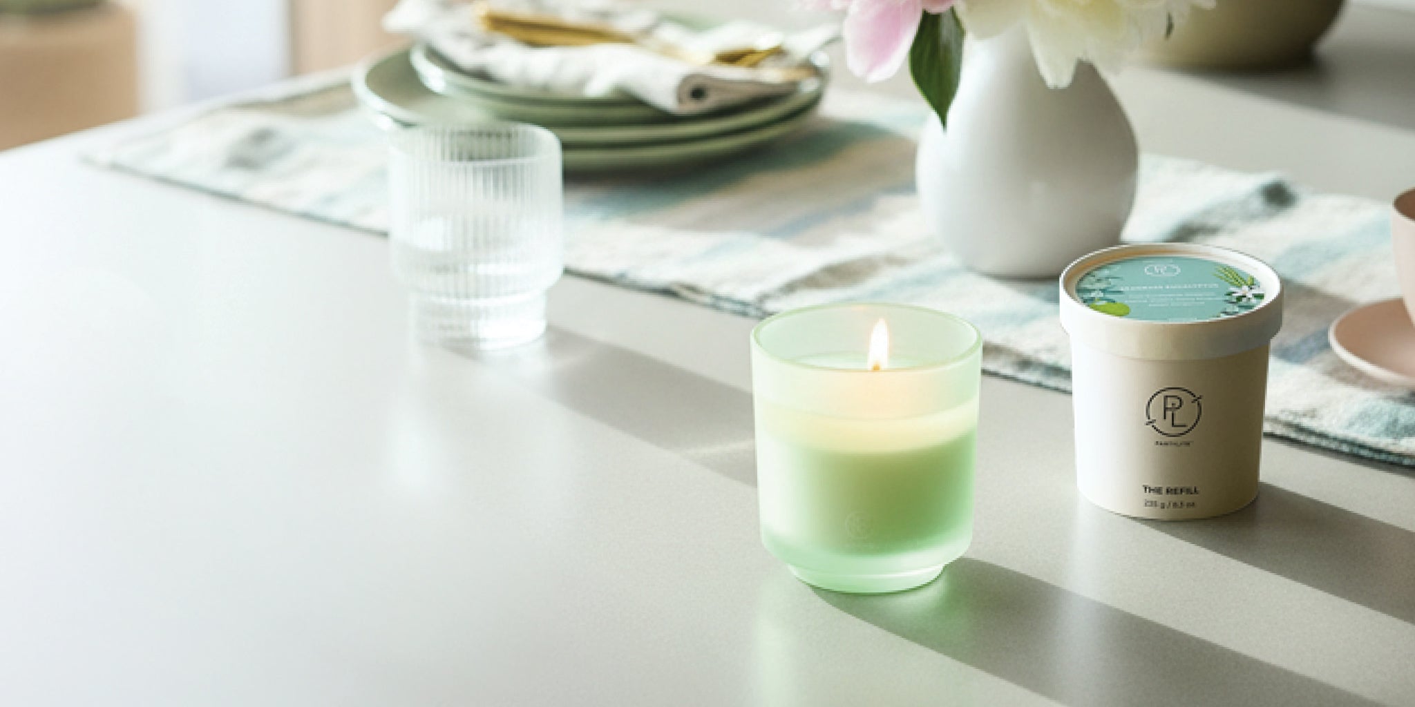 Refillable Jar and refill on a table with table runner, dishes and vase with flowers