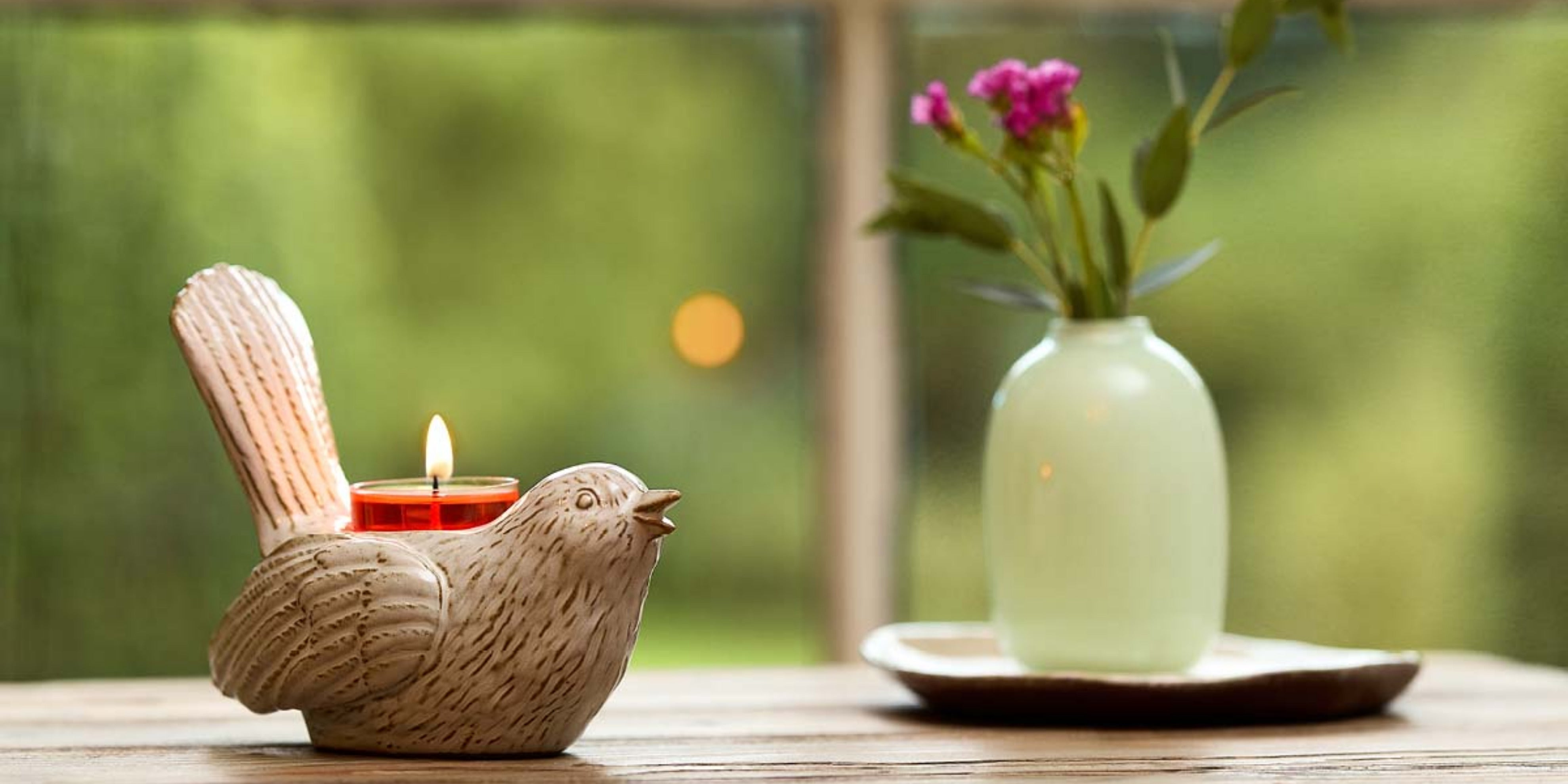 Songbird tealight holder on a wooden table next to vase of flowers on tray