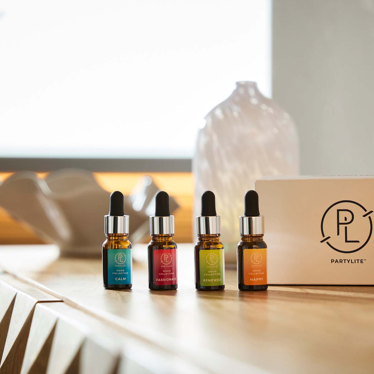 Mood 4-Pack Fragrance Oil Sampler shown on a wooden surface with the box packaging next it against a light background.