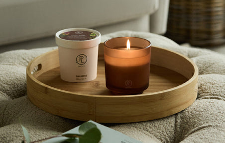 Refillable candle jar and refill candle on a wooden tray with a blurred background of a living room